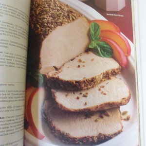 May include: A close-up of a sliced roasted pork loin with a crust of herbs and spices. The pork is on a white platter with slices of peach and basil leaves. The text "Breaded Pork Roast" is visible in the upper right corner of the image.