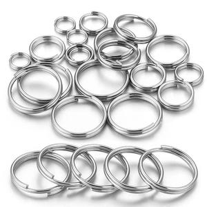 Puede incluir: Una colección de llaveros divididos de color plateado en varios tamaños. Los anillos son de metal y tienen un diseño de doble bucle para mayor durabilidad. Los llaveros están dispuestos en un patrón disperso, mostrando sus diferentes diámetros.