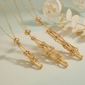 May include: Three gold necklaces with detailed, openwork patterns. Each necklace has a fine chain leading to a decorative pendant with small, sparkling details. The pendants have a geometric, linear structure, creating an elegant and sophisticated appearance.
