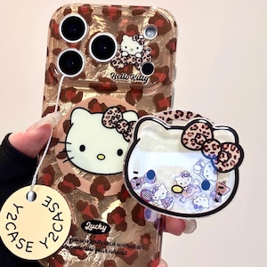 May include: A clear phone case with a leopard print design and a Hello Kitty graphic. The case has a matching Hello Kitty charm with floating confetti inside. The text "Lucky" and "Hello Kitty" are visible.