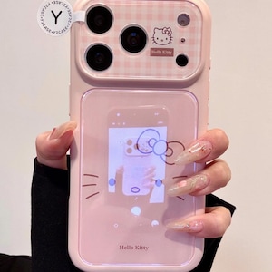 May include: Pink phone case with a Hello Kitty design. The case features a pink and white gingham pattern on the top, the Hello Kitty logo, and a clear section displaying a Hello Kitty graphic. The case has a camera cutout.