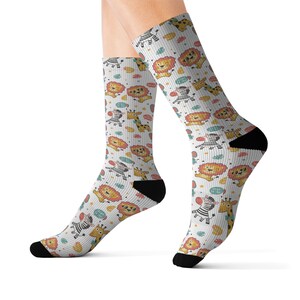 May include: White socks with a repeating pattern of cartoon lions, zebras, and giraffes. The socks have black heels and toes. The design includes colorful accents like blue, yellow, and red.