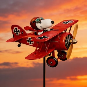 May include: A red biplane wind spinner featuring a cartoon dog character wearing a pilot's helmet and goggles. The plane has black and white markings and a wooden propeller. The background is a colorful sunset.
