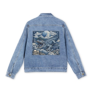 May include: Light blue denim jacket with a detailed graphic on the back. The graphic features a blue alligator with an open mouth, a full moon, and skulls. The jacket has a classic design with button closures and pockets.