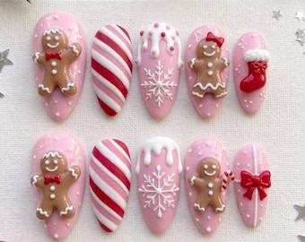 May include: A set of ten almond-shaped press-on nails in a light pink base color. The designs feature 3D gingerbread figures, red and white candy cane stripes, white snowflakes with icing drips, a red Christmas stocking, and a red gift bow.