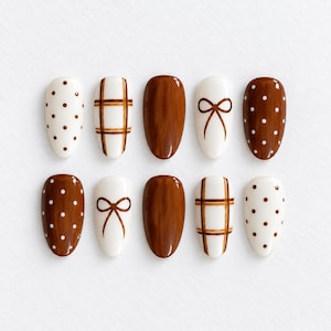 May include: A set of ten almond-shaped press-on nails featuring a brown and white color palette. The designs include solid brown nails, white nails with brown polka dots, brown nails with white polka dots, brown plaid patterns, and brown bow motifs.