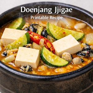 May include: A close-up of a bowl of Doenjang Jjigae, a Korean stew. The stew contains tofu cubes, zucchini slices, red chili peppers, and other vegetables. The text "Doenjang Jjigae Printable Recipe" is displayed at the top of the image.