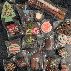 May include: Assortment of individually wrapped chocolate-covered treats, including pretzels, cookies, and candies. The treats are decorated with colorful sprinkles, icing, and festive designs, such as a Christmas tree and ornament.