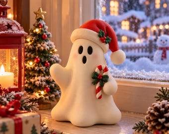 Puede incluir: Una figura de fantasma blanco que lleva un gorro de Papá Noel rojo con borde blanco y una ramita de acebo. El fantasma tiene una expresión de sorpresa con ojos negros y boca ovalada, sosteniendo un bastón de caramelo rojo y blanco.