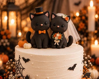 Puede incluir: Un pastel blanco decorado con dos figuras de gatos negros, uno con sombrero de copa y pajarita naranja, el otro con velo blanco y ramo de flores. El pastel tiene adornos de telarañas negras, murciélagos y pequeñas calabazas naranjas y blancas.