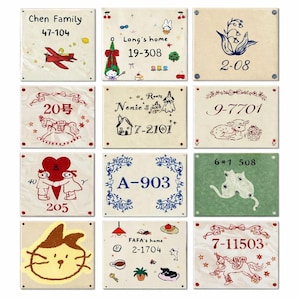 Könnte beinhalten: Eine Sammlung von zwölf dekorativen Keramikfliesen, jede mit einzigartigen handgezeichneten Illustrationen und Texten. Designs umfassen ein rotes Flugzeug, ein Kaninchen, ein Lamm und eine Katze. Die Fliesen sind cremefarben mit verschiedenen Text- und Zahlenkombinationen.