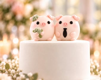 Puede incluir: Dos figuras de cerditos redondos de color rosa claro se sitúan sobre un pastel blanco liso. El cerdito de la izquierda lleva un pequeño tocado floral verde y sostiene un ramo a juego. El de la derecha lleva una corbata negra. Ojos negros y hocicos rosas.