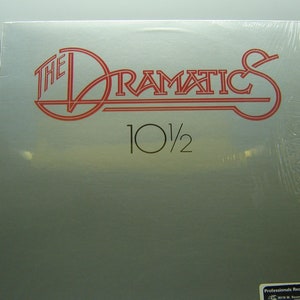 Può includere: Un album di vinile argentato con un logo rosso e bianco che dice "The Dramatics 10 1/2". L'album è avvolto in plastica.