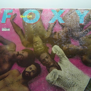 Pu&ograve; includere: Una copertina di un album in vinile con il titolo "FOXY" in grandi lettere blu e le parole "Get Off" in lettere blu pi&ugrave; piccole. La copertina presenta un gruppo di uomini sdraiati su uno sfondo rosa.