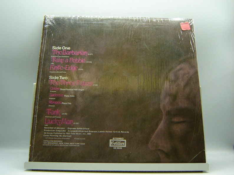 K&ouml;nnte beinhalten: Ein braunes Vinyl-Schallplattencover mit einem Foto eines M&auml;nnergesichts. Das Album tr&auml;gt den Titel "Tank" von "Lucky Man" und enth&auml;lt die Songtitel "The Barbarian", "Take a Pebble", "Knife-Edge", "The Three Fates", "Clytemnestra", "Ladness", "Aroopa", "Tank" und "Lucky/Man".