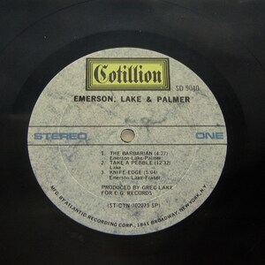 K&ouml;nnte beinhalten: Ein wei&szlig;es Vinyl-Schallplattenlabel mit schwarzem Text. Das Label ist f&uuml;r das Album "Emerson, Lake & Palmer" von Cotillion Records. Die Albumnummer ist SD 9040. Die Schallplatte ist Stereo und Seite eins. Die Trackliste enth&auml;lt "The Barbarian", "Take a Pebble" und "Knife-Edge".