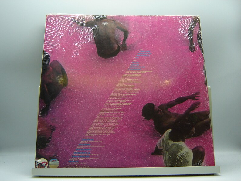 Pu&ograve; includere: Copertina di un album in vinile rosa con una foto di persone in acqua. Il titolo dell'album &egrave; "7" e l'artista &egrave; "Fleetwood Mac".
