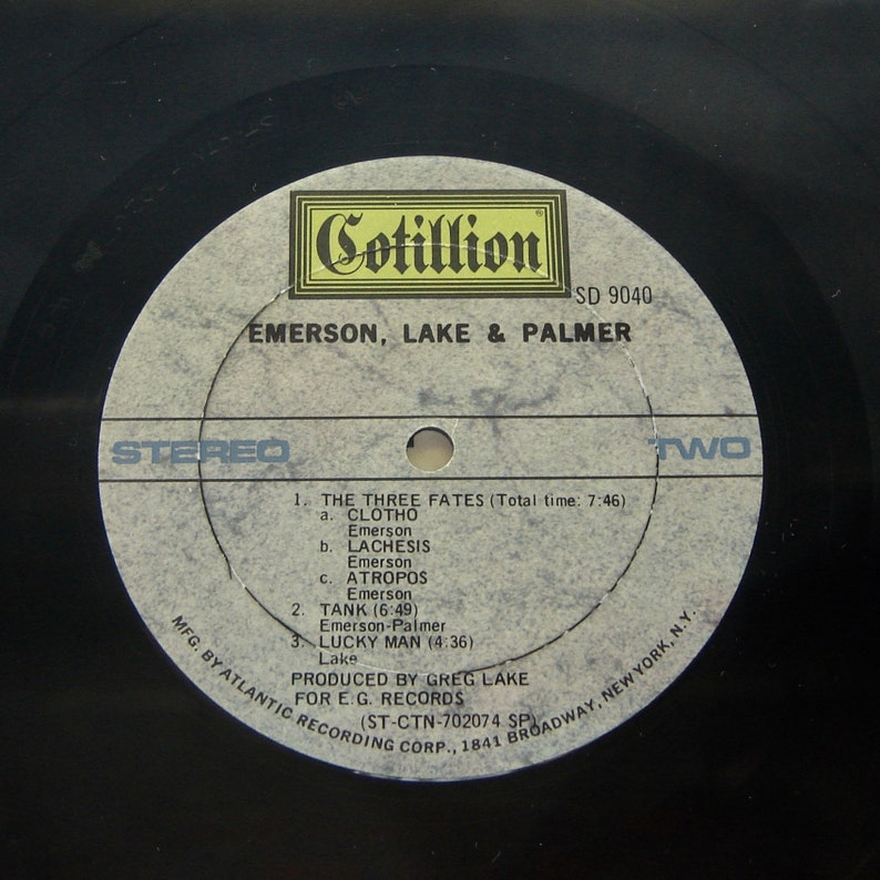 K&ouml;nnte beinhalten: Eine schwarze Schallplatte mit einem wei&szlig;en Label. Das Label zeigt den Text "Cotillion" in einem gelben Kasten, "SD 9040", "Emerson, Lake & Palmer", "Stereo", "Zwei" sowie die Songtitel und K&uuml;nstler. Das Label zeigt auch den Text "MFG. BY ATLANTIC RECORDING CORP., 1841 BROADWAY, NEW YORK, N.Y.", "PRODUCED BY GREG LAKE FOR E.G. RECORDS (ST-CTN-702074 SP"