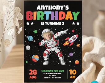 Puede incluir: Una tarjeta de invitación de cumpleaños rectangular con fondo negro y temática espacial. El texto dice Anthony's Birthday is turning 3. Una ilustración central muestra a un astronauta con la cara de un niño, un cohete y planetas.