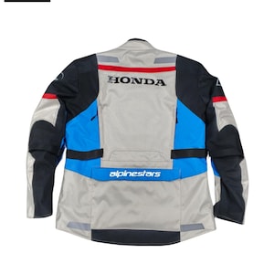 May include: Motorcycle jacket in gray, black, and blue with the "HONDA" logo across the back. The jacket features reflective stripes and the "alpinestars" logo. The jacket is designed for motorcycle riding.