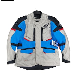 May include: A motorcycle jacket in gray, blue, black, and red. The jacket has the Honda logo and the Alpinestars logo. It has multiple pockets and a Drystar label.