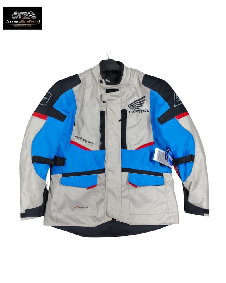 May include: A motorcycle jacket in gray, blue, black, and red. The jacket has the Honda logo and the Alpinestars logo. It has multiple pockets and a Drystar label.
