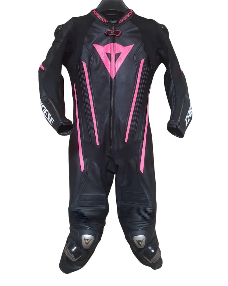 Puede incluir: Traje de carreras de moto negro con detalles en rosa. El traje tiene una cremallera completa, protecciones en rodillas y hombros, y la marca "DAINESE" impresa en las mangas. Un logotipo rosa est&aacute; en el pecho.