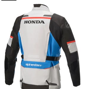 May include: Motorcycle jacket with a white, black, and blue color scheme. The jacket features the "HONDA" logo across the back, with "alpinestars" branding below. The jacket has a high collar and a belt at the waist.
