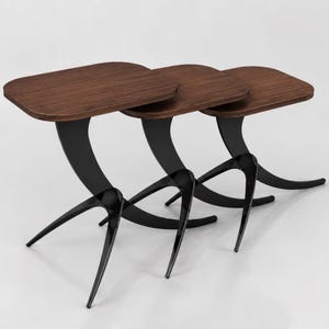 May include: Set of three nesting tables. Each table has a dark brown, rectangular top with rounded corners. The legs are black, with a curved design and three pointed feet. The tables are arranged in a row, with the smallest table nested under the larger ones.