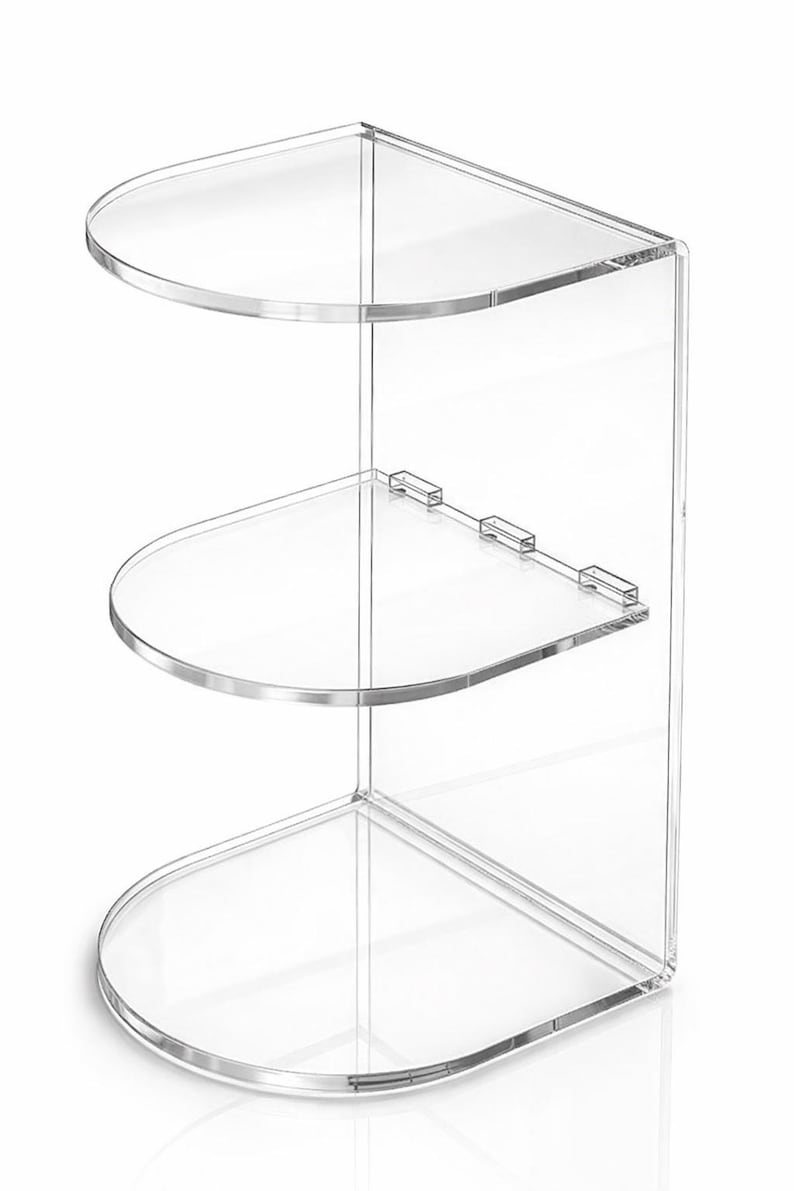 May include: Clear acrylic corner shelf with three rounded shelves. The shelves are connected by a clear vertical support. The design is modern and minimalist, suitable for displaying items in a bathroom or living space.