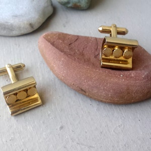 Può includere: Un paio di gemelli d'oro con un design testurizzato. Ogni gemello ha tre accenti rotondi in oro.