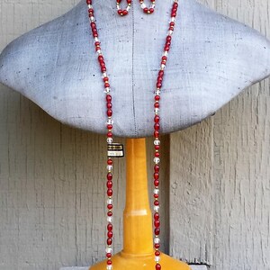 May include: A red and clear glass beaded necklace and matching earrings on a mannequin. The necklace is long and hangs down to the mannequin's waist. The earrings are small and dangle.