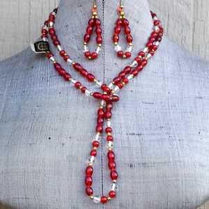 May include: A red and clear glass beaded necklace and matching earrings with gold accents. The necklace is long and has a tassel at the end.