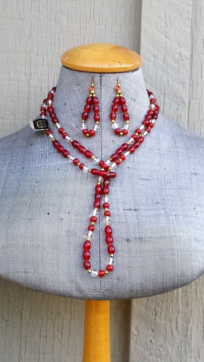 May include: A red and clear glass beaded necklace and matching earrings with gold accents. The necklace is long and has a tassel at the end.