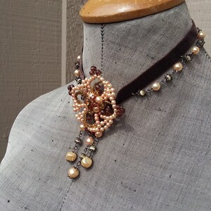 May include: A brown velvet choker necklace with a delicate beaded pendant featuring a floral design in shades of peach and brown.