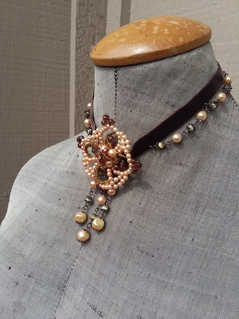 May include: A brown velvet choker necklace with a delicate beaded pendant featuring a floral design in shades of peach and brown.