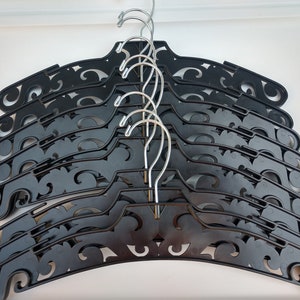 May include: A stack of black plastic hangers with decorative swirls. The hangers have silver metal hooks.