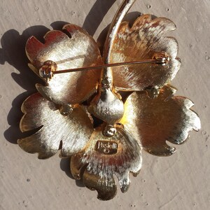 May include: Gold-toned flower brooch with a pin on the back. The brooch is marked "Pascucci" on the back.