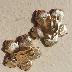 May include: A pair of gold-tone flower-shaped clip-on earrings with the word "Pascielli" engraved on the back.