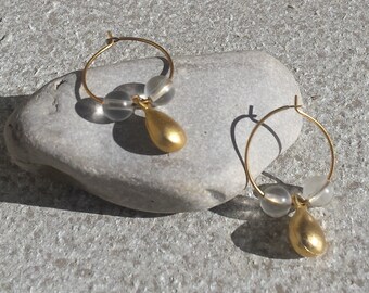Piccoli orecchini a cerchio minimalisti in metallo color oro con perlina trasparente e ciondolo a goccia in oro. Gioielli pendenti.