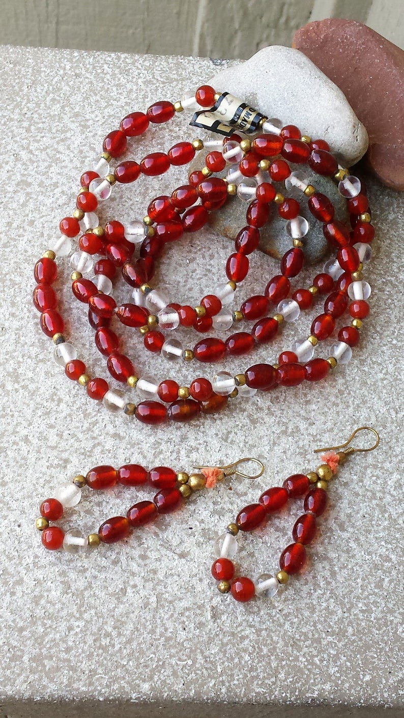 May include: A red carnelian and clear glass bead necklace with gold accents and matching earrings. The necklace is layered and has a vintage feel.