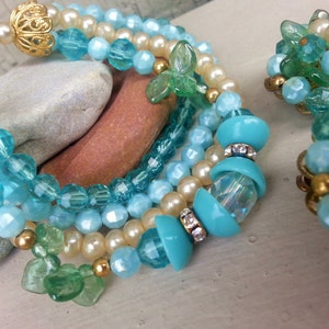May include: A multi-strand bracelet and earrings set featuring turquoise and green glass beads. The bracelet has a gold clasp and a large turquoise bead with rhinestones. The earrings are cluster style with green and turquoise beads.