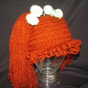 May include: A crocheted hat with long, orange yarn hair and two green bows on top.