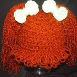 May include: A crocheted hat with long, red yarn pigtails and two white crocheted bows on top.