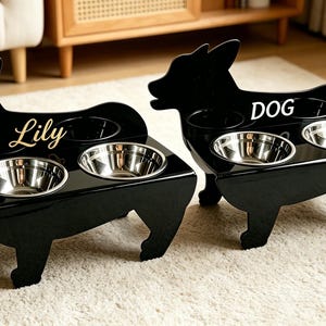 May include: Two black dog-shaped pet feeders with stainless steel bowls. One feeder has the name "Lily" in gold script, the other has the word "DOG". The feeders are on a light-colored rug.