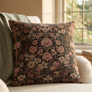 May include: A square throw cushion featuring a dark brown background with a dense, woven tapestry pattern of muted pink, peach, and cream-coloured floral motifs, including roses and various small blossoms arranged in a symmetrical botanical design.