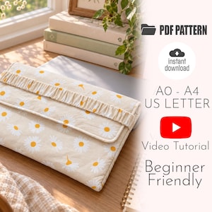 May include: A rectangular fabric laptop sleeve featuring a cream background with a white and yellow daisy floral pattern. The sleeve has a horizontal pleated fabric strap across the front flap. Text includes PDF PATTERN, instant download, A0 - A4 US LETTER, Video Tutorial, and Beginner Friendly.