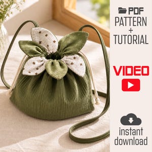 May include: A green drawstring pouch with a flower-shaped top featuring white and green floral fabric petals. The bag has long green straps and includes text reading PDF PATTERN + TUTORIAL, VIDEO, and instant download on the right side.