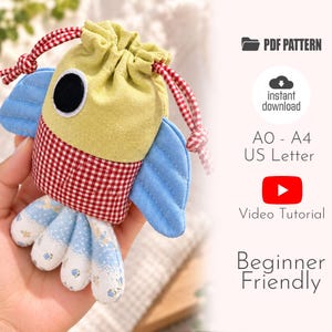 May include: A fabric drawstring pouch shaped like a fish with a yellow head, red and white checkered body, blue fins, and a light blue floral tail. Text includes PDF PATTERN, instant download, AO - A4 US Letter, Video Tutorial, and Beginner Friendly.