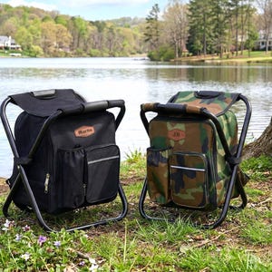 May include: Two portable folding chair backpacks with black metal frames. One is solid black with a brown leather-style patch reading Martin, and the other features a green, brown, and black camouflage pattern with a patch reading JH.
